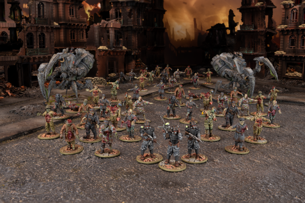 A diorama scene of numerous miniature soldiers in a ruined city with two large crab like mechs looming behind them in the smoky orange lit background