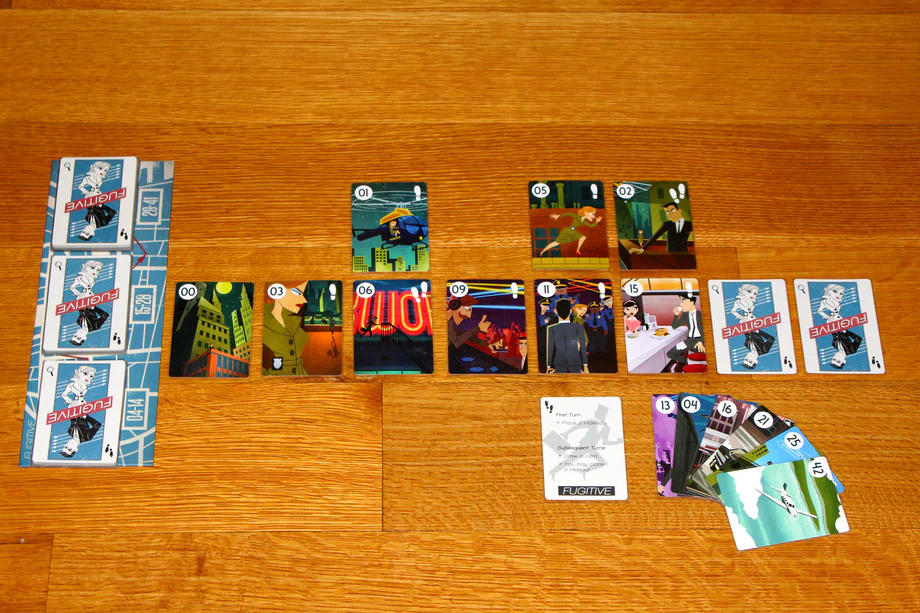 image Frontline Gaming Board game in progress on a wooden table blue backed deck on the left a row of numbered character cards in the center and a small pile of cards on the right