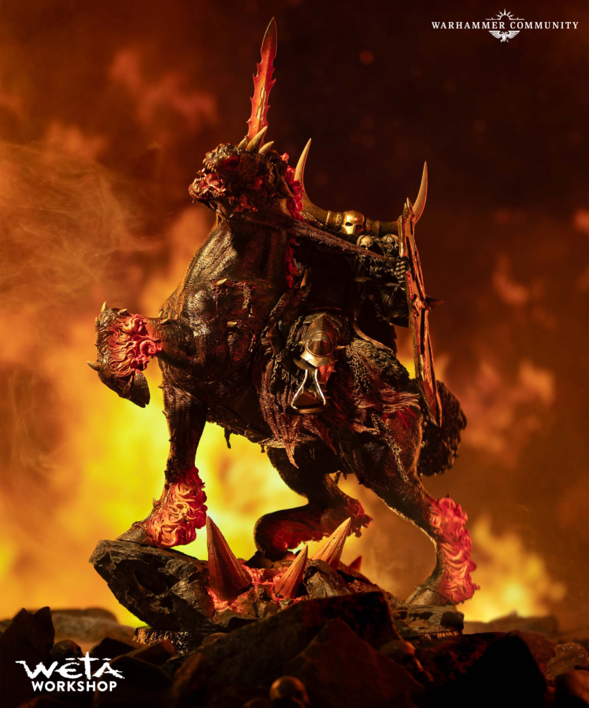 Fiery lit demonic creature perched on jagged rocks amid lava with Warhammer Community logo top right and Weta Workshop bottom left