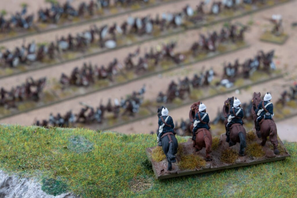 image Frontline Gaming Miniature cavalry on a grassy slope with a detailed battlefield diorama in the background