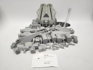 Grey plastic sci fi tank and weapon model display on a white surface with a price tag nearby