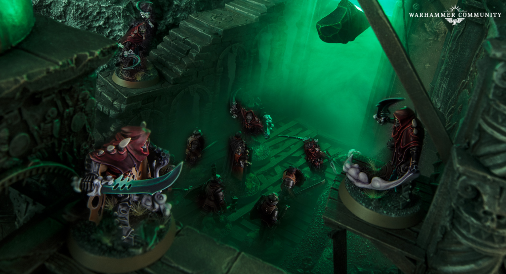 image Frontline Gaming Warhammer miniatures clash in a ruined dungeon with green fog, crimson-clad figures surrounding a glowing orb at center.