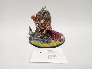 Painted tabletop miniature of a demonic creature crouching on a ruined stone pedestal with tufts of yellow grass displayed on a circular base with a price tag nearby