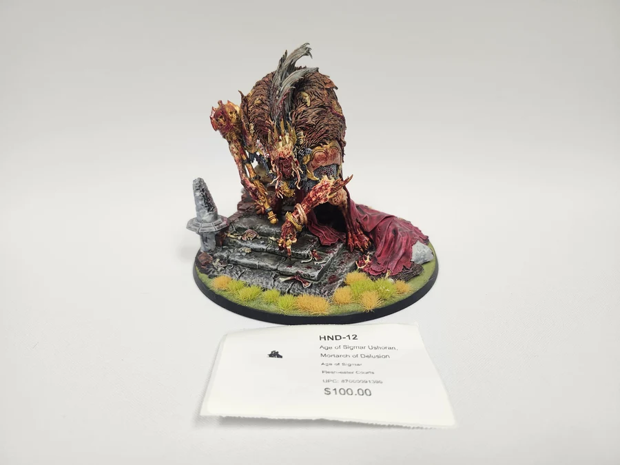 Painted tabletop miniature of a demonic creature crouching on a ruined stone pedestal with tufts of yellow grass displayed on a circular base with a price tag nearby