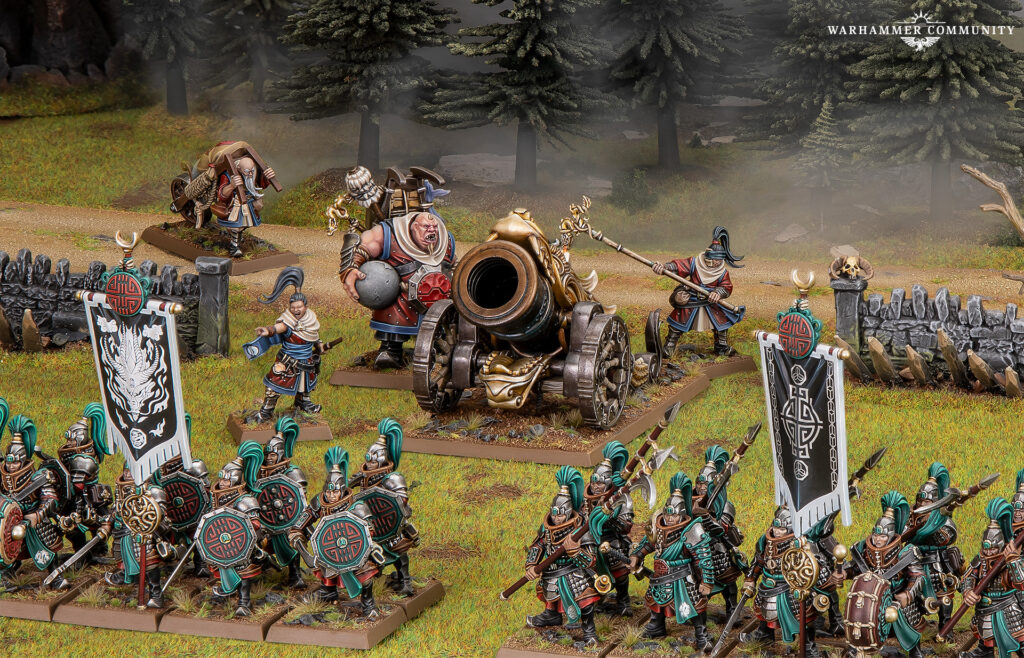 Massed Warhammer miniatures clash in a grassy field teal armored infantry advance toward a central ornate cannon with banners and a stone fence in the foreground