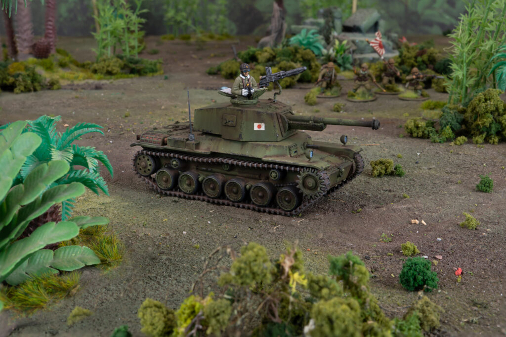 Miniature green tank with a soldier figure on top in a woodland diorama with tiny trees and shrubs nearby