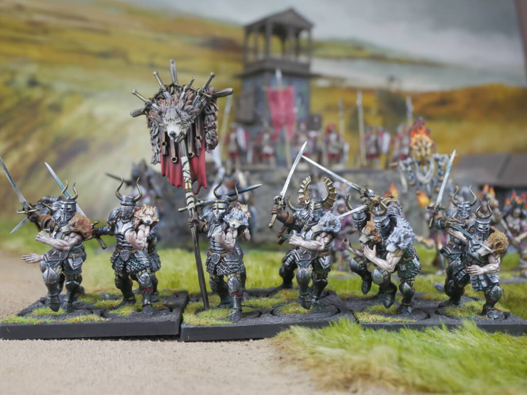 Tabletop wargaming miniature army advancing with swords and a banner setup on grassy bases with a distant fortress backdrop