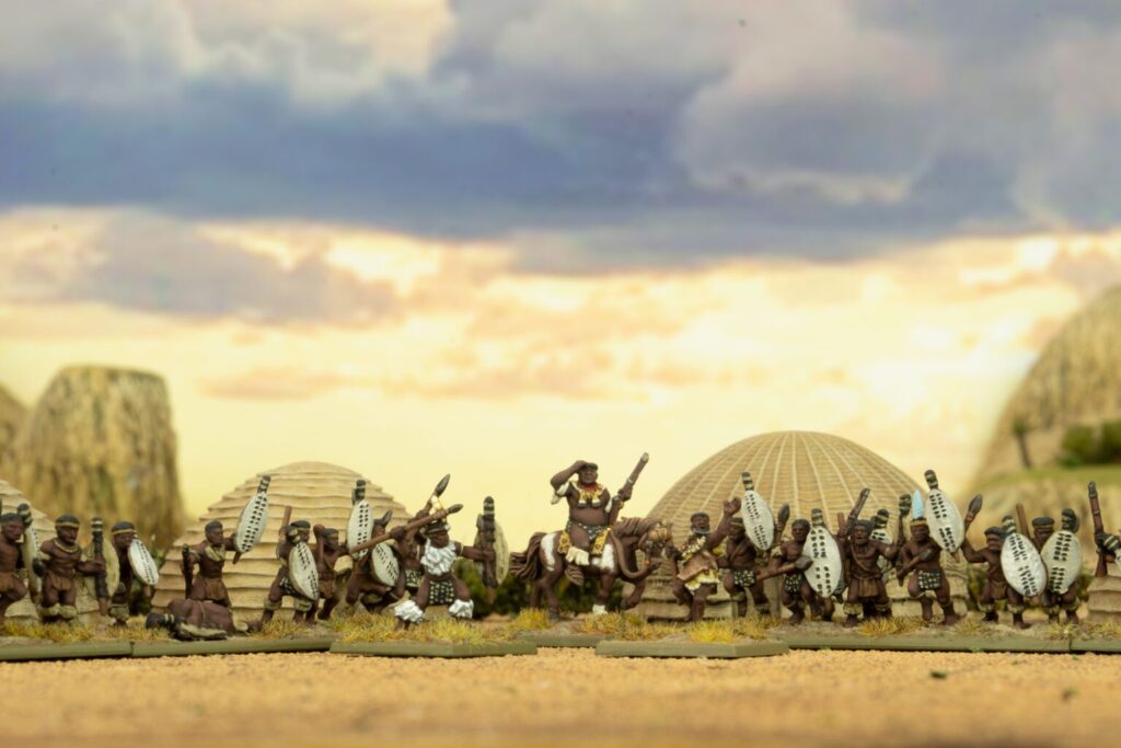 Projecttrain0241536x1024 Frontline Gaming Row of miniature fantasy warriors with round shields marching in a desert village diorama central figure on a horse holding a spear or sword