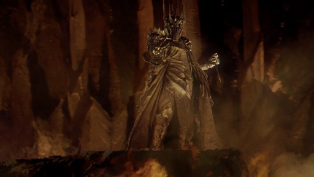 Dark armored figure with a raised arm stands on a rocky ledge in a fiery cavern filled with smoke and lava glow