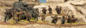 Group of toy soldiers advancing with a model tank in a rocky grassy diorama scene military miniature display