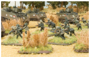 Scale model diorama of WWII US Army tanks and infantry advancing through tall grass field