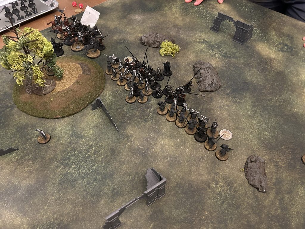 Tabletop wargame scene with two marching squads of metal miniatures facing each other trees rocks and ruined walls on a textured gaming mat