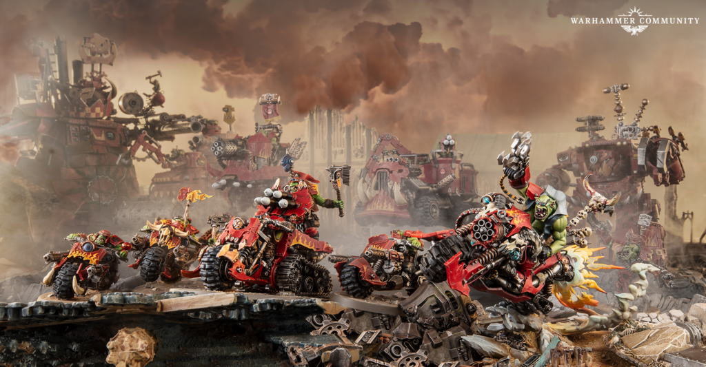 Red Warhammer war machines clash on a smoky rubble strewn battlefield as orks charge Warhammer Community logo top right