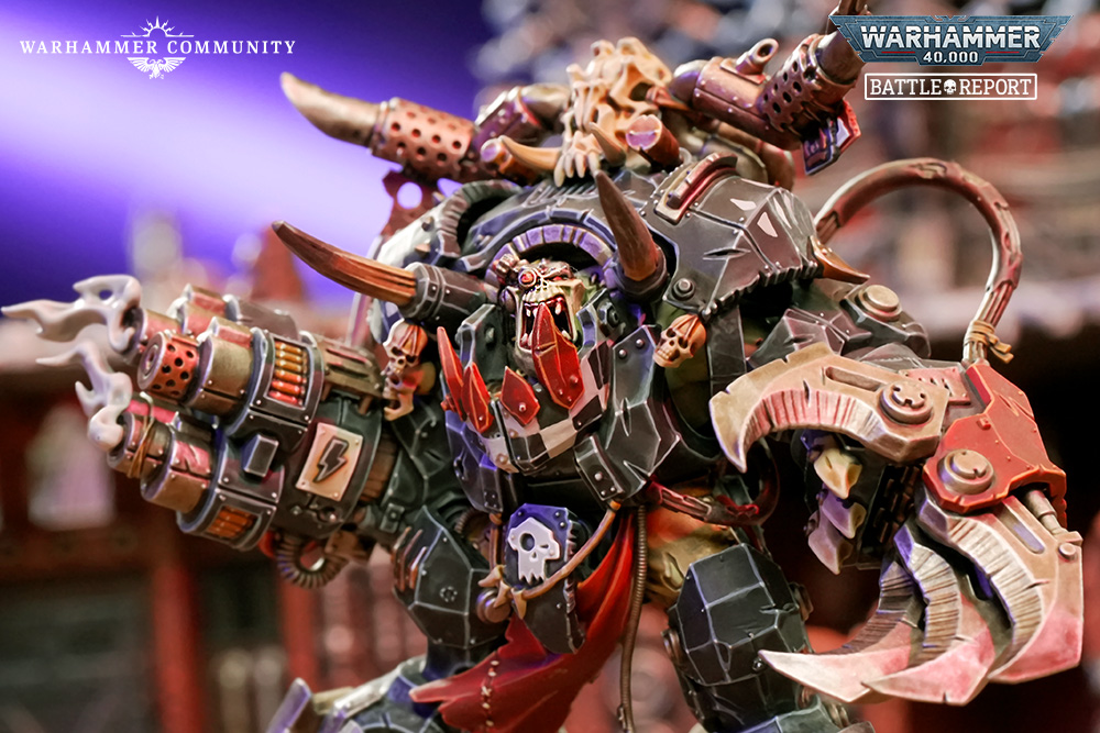 image Frontline Gaming Large painted Warhammer 40000 warboss miniature with heavy armor and oversized claw weapons on display Warhammer Community and Battle Report logos visible at top corners