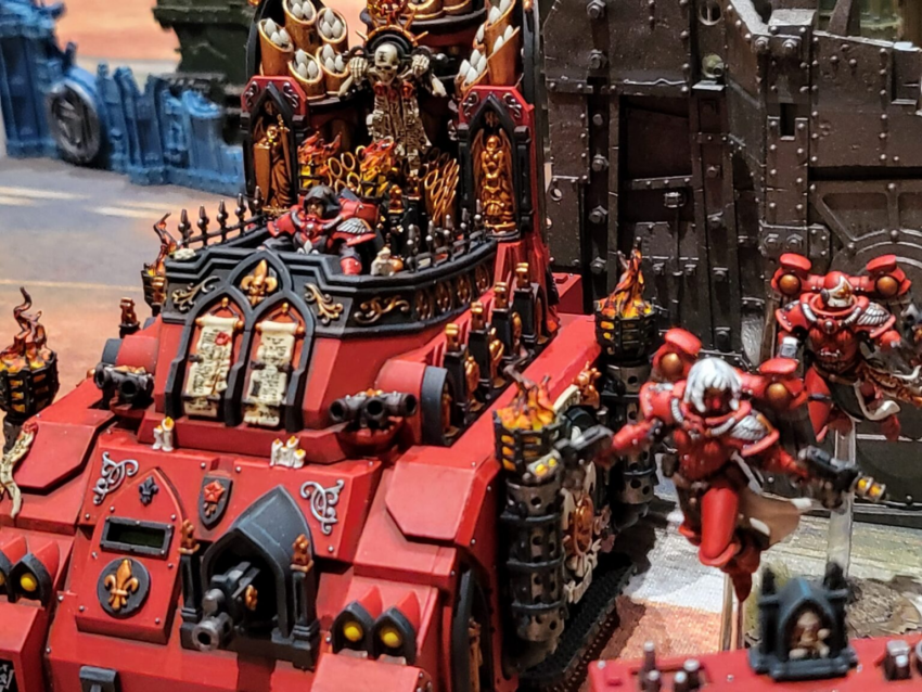 image Frontline Gaming Red heavily armored Warhammer style battle tank with black and gold Gothic trim skull insignia and red clad miniatures on and around it in a tabletop diorama LVO Interview