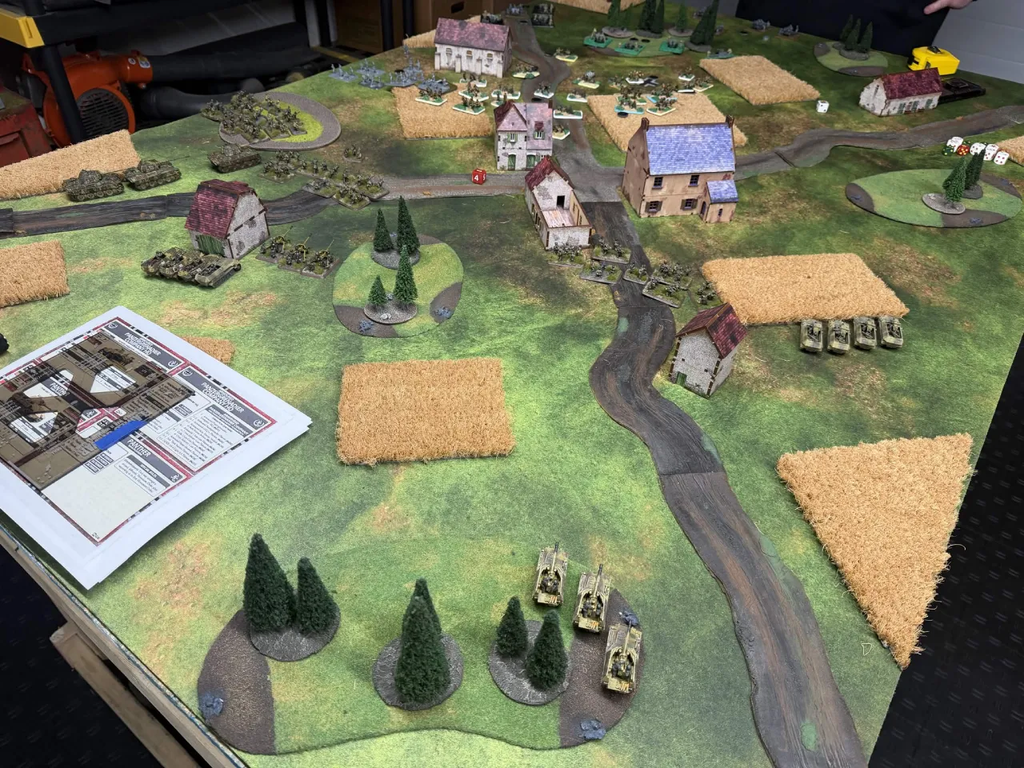 Tabletop wargaming battlefield with miniature village tanks roads and fields on a green mat