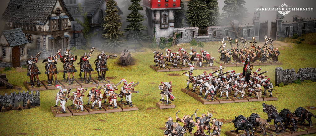 Tabletop Warhammer battle scene with multiple regiments clashing on a grassy battlefield amid ruined buildings and trees plus a distant logo in the corner