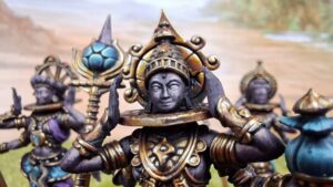 Close up of ornate fantasy figurines central dark statue wearing a gold headdress and circular collar hands raised to either side with others in the background