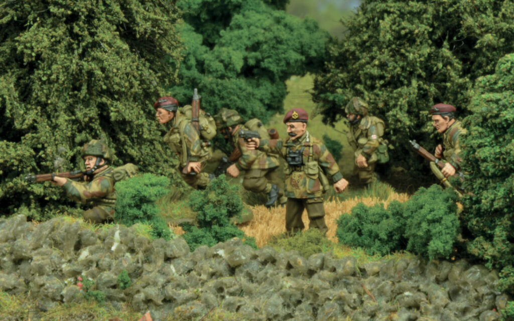 FoFBritishAirborneArticleHeader11536x960 Frontline Gaming Group of camouflaged soldiers advancing through a hedged field behind a stone wall guns ready