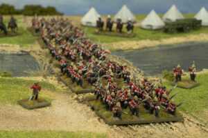 Miniature soldiers in red coats marching in formation across a dirt path by a river, with tents and a wagon in the background, as part of a diorama battle scene