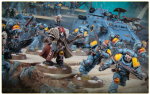 Tabletop battle scene with blue-armored Space Marines clashing with a dark-clad commander and a large armored vehicle in the background.