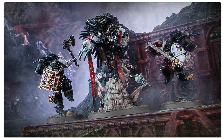 Three elaborately painted Warhammer 40k Space Marines figures posed on a rocky diorama with a red train car backdrop