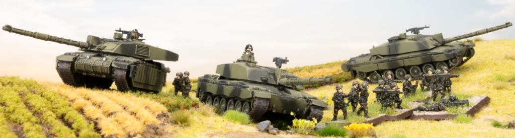 Plastic toy tanks and soldiers arranged on a grassy diorama with three tanks and a group of figures in a sunlit field