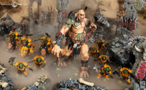 Massive orc warboss leads waves of green skinned orcs in yellow armor through a smoky ruined battlefield with crumbling arches and rocks