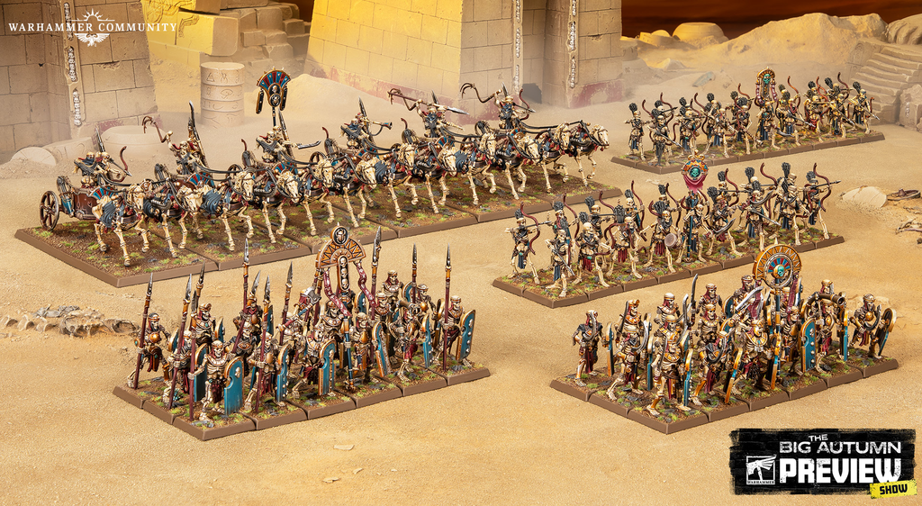 Wargaming miniatures arrayed for battle on a sandy desert battlefield amid ancient ruins with chariots and banners visible