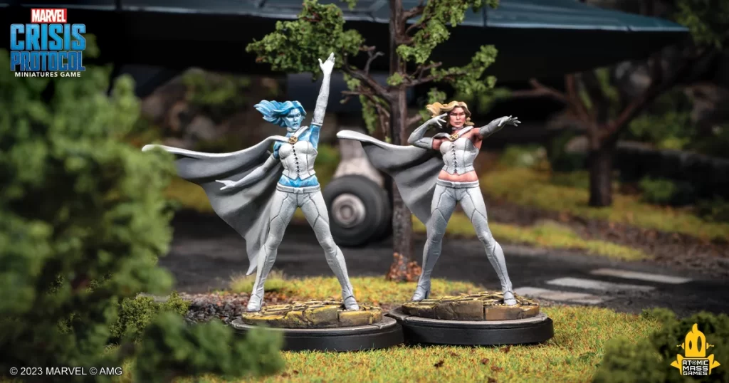 painted emma Frontline Gaming Two Marvel Crisis Protocol miniatures in silver outfits with capes strike dynamic poses on round bases in a grassy diorama