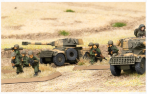 Miniature army scene with toy soldiers advancing beside camouflaged tanks on a desert diorama