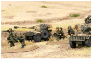 Toy soldiers advancing with model tanks on a sandy diorama battlefield.
