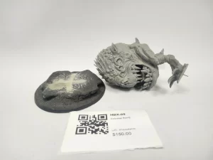Gray resin miniature of a monstrous squid headed creature with jagged teeth lying beside a round base on a white backdrop